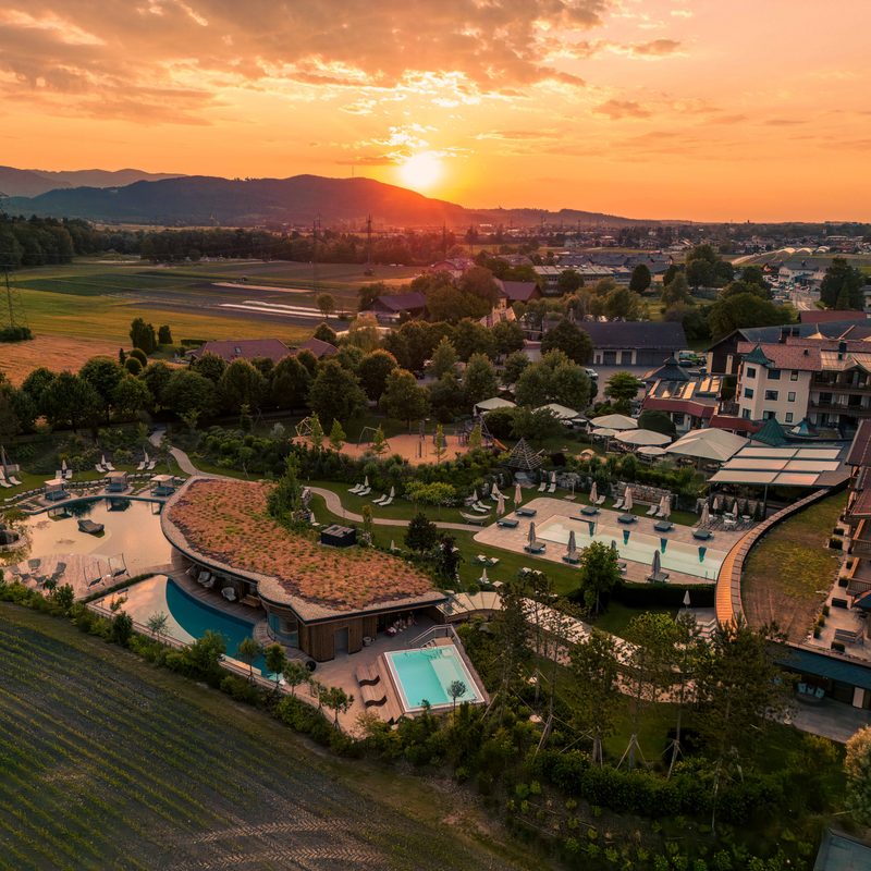 Luftaufnahme einer Hotelanlage mit Poollandschaft und Gärten bei Sonnenuntergang.