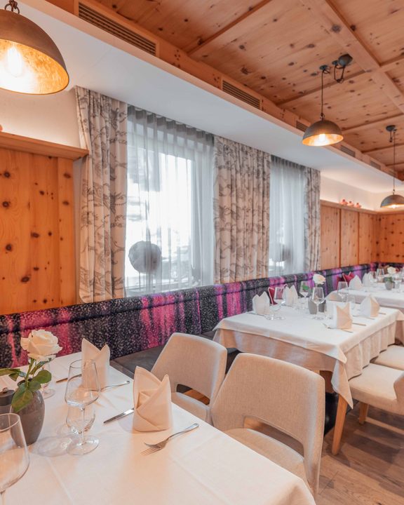 Gedeckte Restauranttische mit Gläsern und gefalteten Servietten in einem hellen Speisesaal mit Holzdecke.