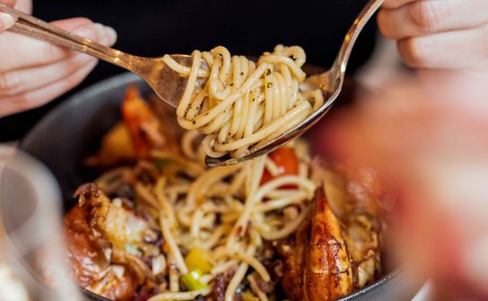 Person eating spaghetti with prawns from a bowl.