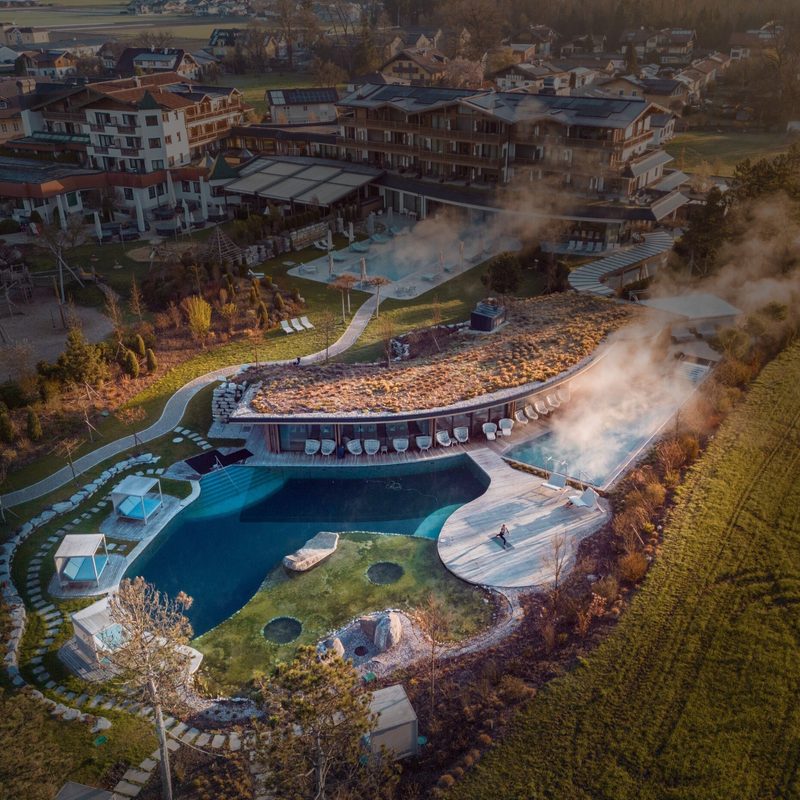 Drohnenaufnahme einer Hotelanlage mit Wellnessbereich, beheiztem Außenpool und Dampfwolken.