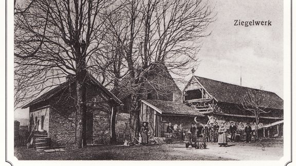 Historic black-and-white photo of a brickyard with buildings, leafless trees, and a group of people in the yard.