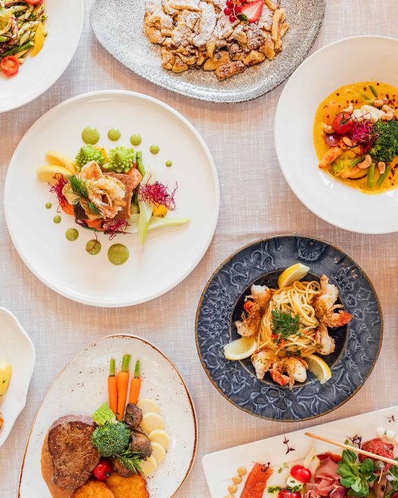 Mehrere Gourmetgerichte auf Tellern auf einem Restauranttisch, fotografiert von oben.