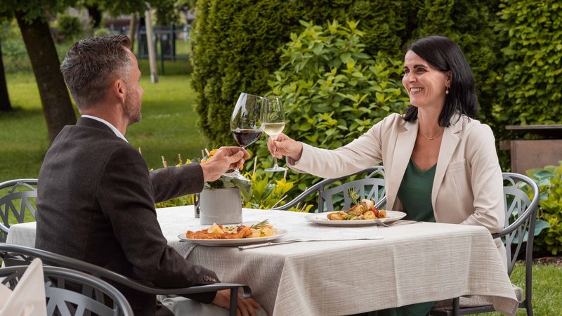 Ein Paar stößt mit Wein auf der Restaurantterrasse im Garten an.