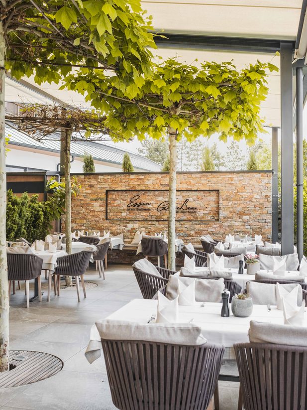 Gedeckte Tische auf einer überdachten Restaurantterrasse unter rankenden Reben im Garten.