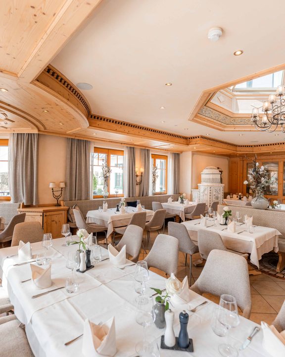 Heller Restaurant-Speisesaal mit gedeckten Tischen, Polsterstühlen und Kronleuchtern.