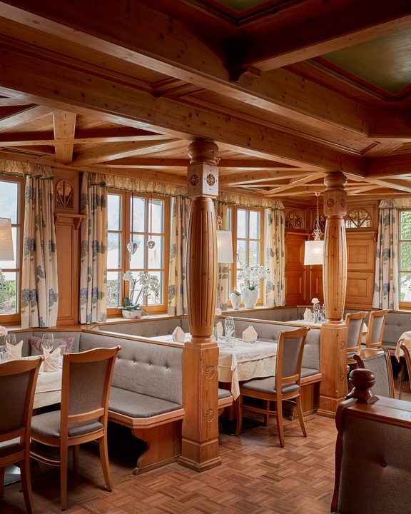 Rustikaler Restaurantbereich mit Holzdecke, gedeckten Tischen, Polsterbänken und großen Fenstern.