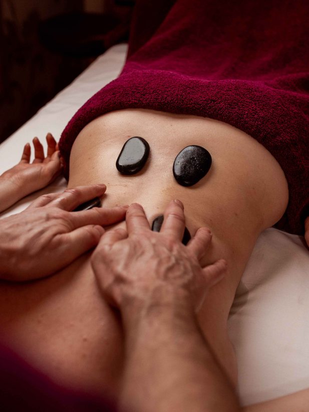 Staff member places warm stones on a guest’s back during a hot stone massage.