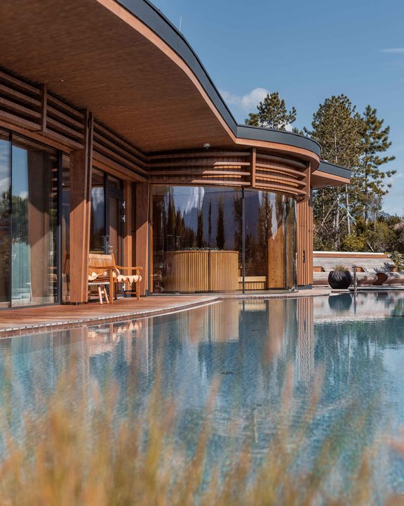 Moderner Hotelaußenbereich mit Pool, Holzfassade, Glasfront und Liegen an der Terrasse.