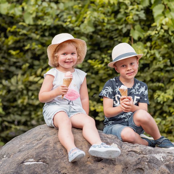 Zwei Kinder sitzen auf einem großen Stein im Garten und essen Eis in der Waffel.
