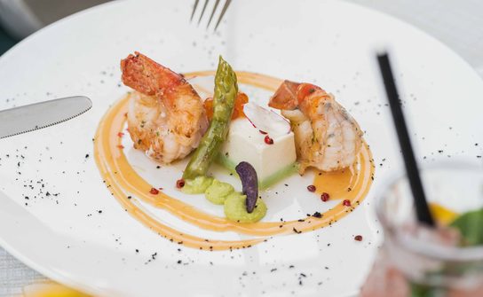 Fine dining plate with two prawns, green asparagus and sauce on a white porcelain plate.