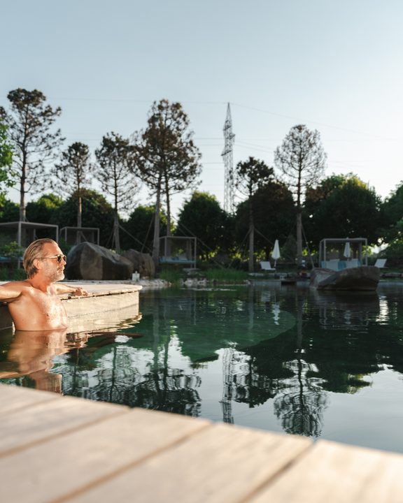 A guest relaxes at the edge of an outdoor pool in a garden area.