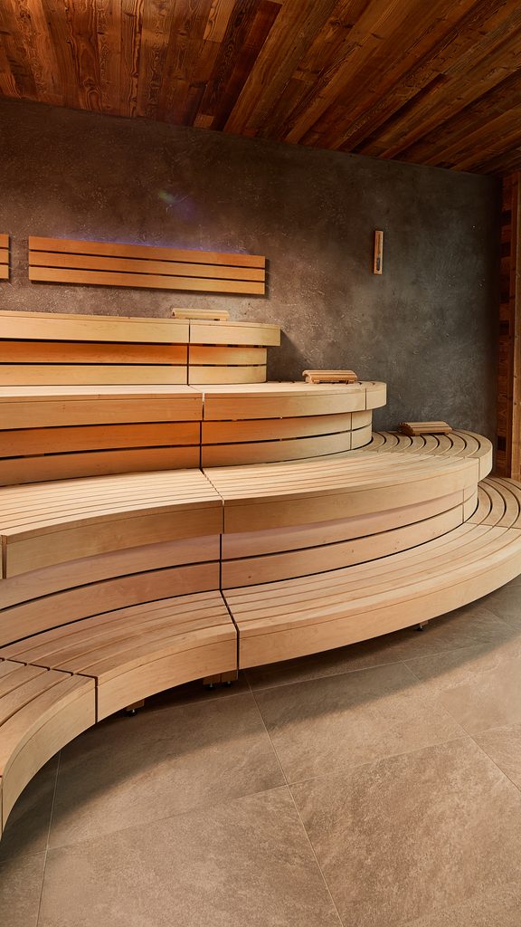Moderne Holzsauna mit geschwungenen Sitzbänken und Glasfront zur Terrasse.