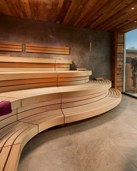 Modern wooden sauna with curved benches and a glass front opening to the terrace.