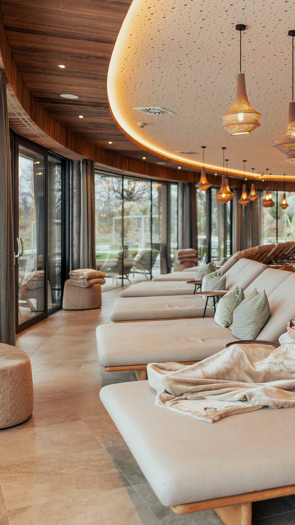 Frau entspannt auf Liege im Wellness-Ruheraum vor großer Glasfront.