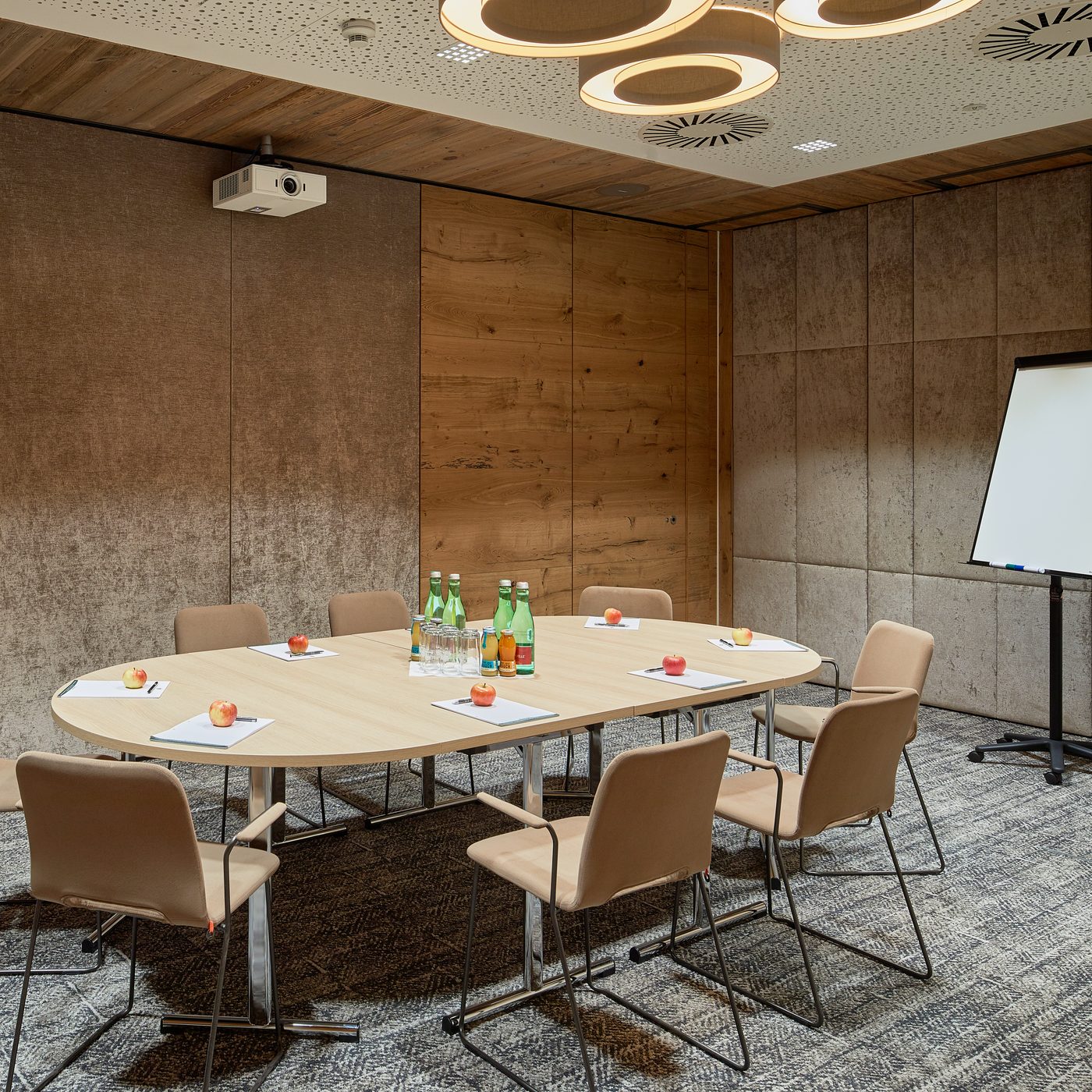 Meeting room with round table, chairs, flip chart, water bottles and a ceiling projector.