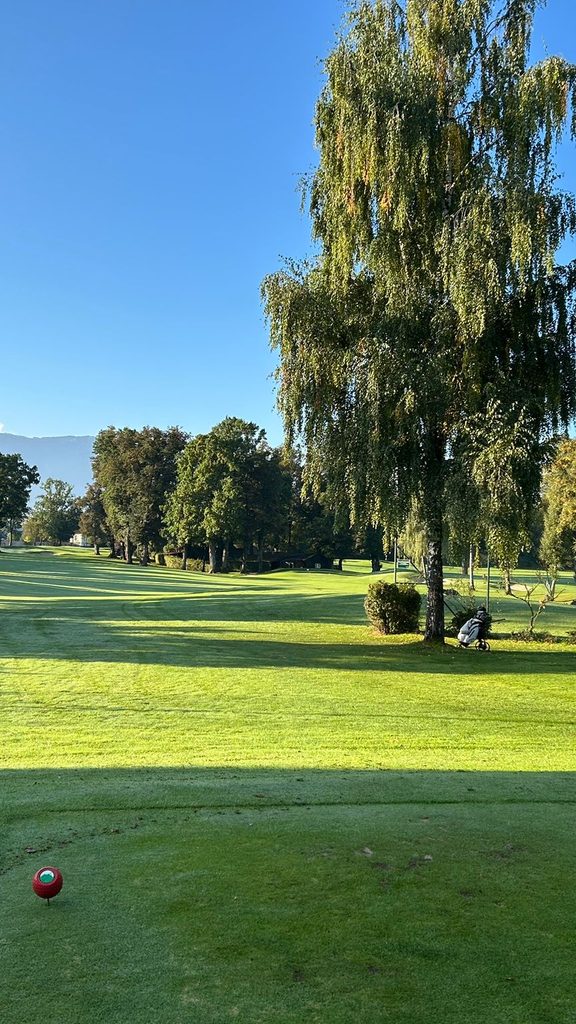 View from a golf tee over a fairway with trees and mountains in the background.