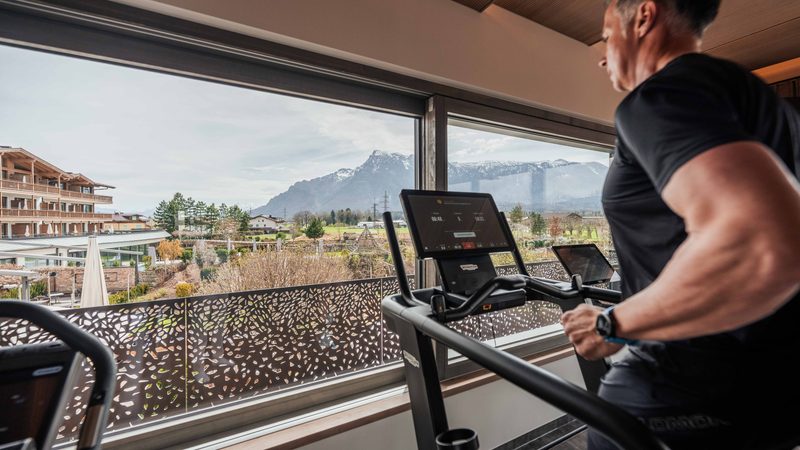 Guest running on a treadmill in a gym by large windows with views of mountains and the hotel grounds.