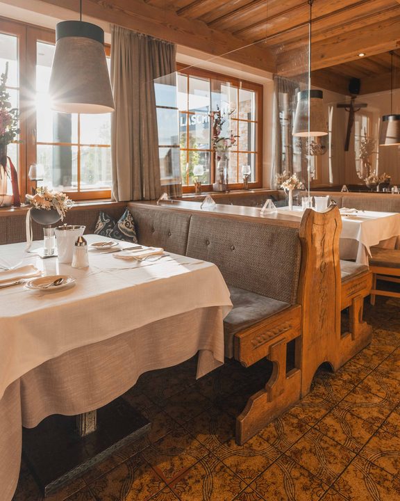 Rustikale Restaurant-Sitzecke mit gedeckten Tischen, Lederbank, Holzstühlen und großen Fenstern.