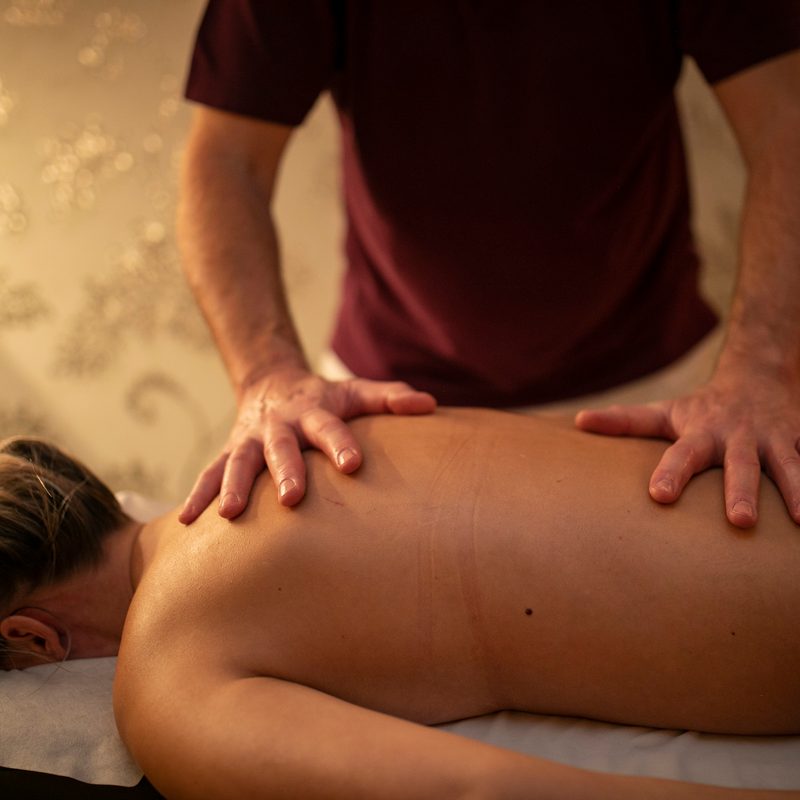 Mitarbeiter massiert den Rücken eines Gastes auf einer Massageliege im Wellnessbereich.