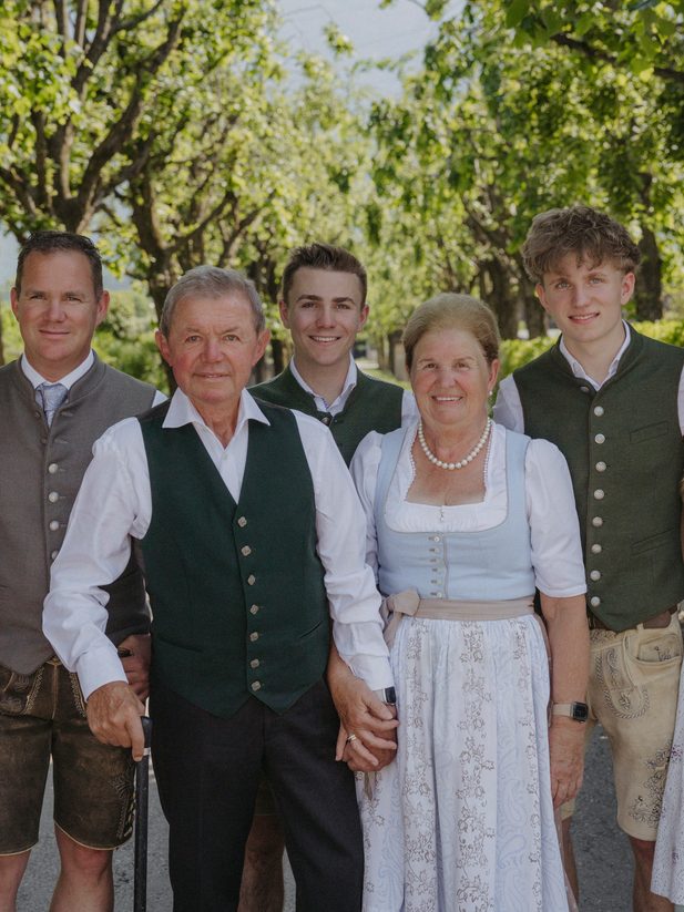 Group portrait of hotel staff in traditional attire on a path in a garden with trees.
