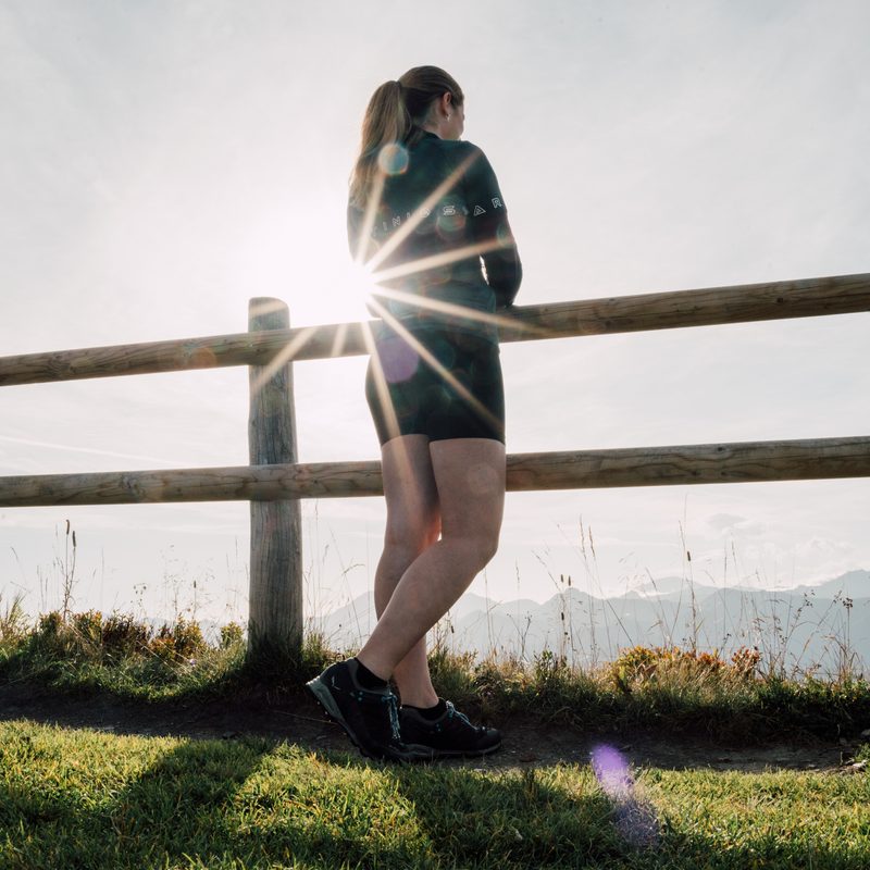 Woman in sportswear leans on a wooden fence with mountain view in backlight.