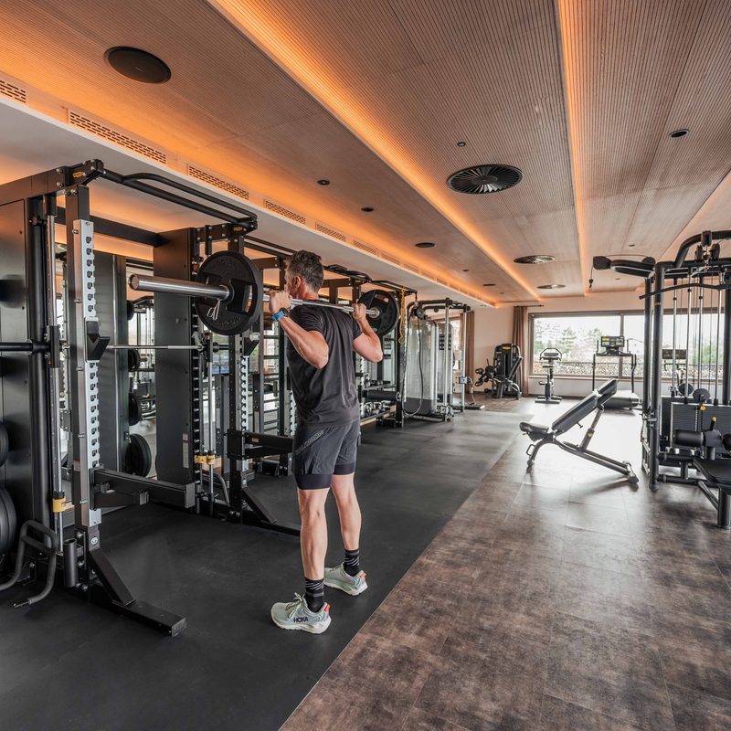 Guest performs barbell squats in a hotel gym with mirrors and strength machines.