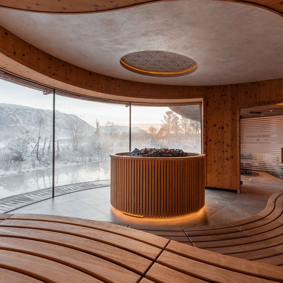 Wellnessbereich mit Sauna, Holzbänken und Panoramafenster mit Blick auf verschneite Landschaft.