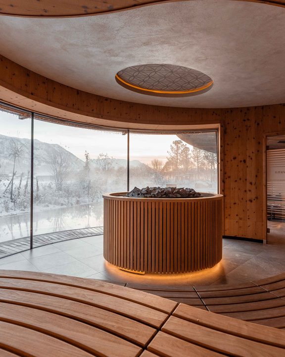 Wellnessbereich mit Sauna, Holzbänken und Panoramafenster mit Blick auf verschneite Landschaft.