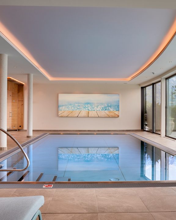 Modernes Hallenbad mit Poolleiter und großen Panoramafenstern mit Blick auf die Berge.