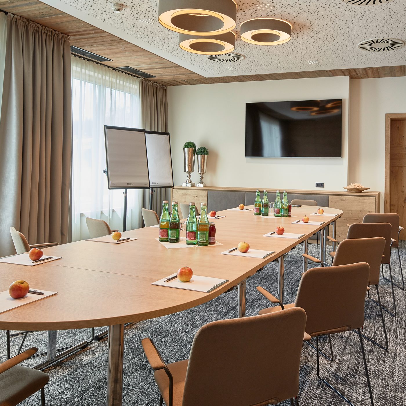 Meeting room with U-shaped table setup, flip chart, screen, and water bottles with fruit.