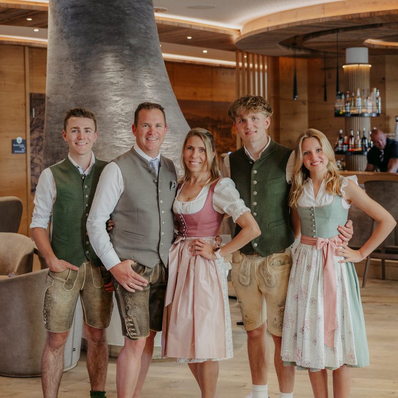 Five staff members in traditional attire stand in a hotel lobby in front of a bar and fireplace.