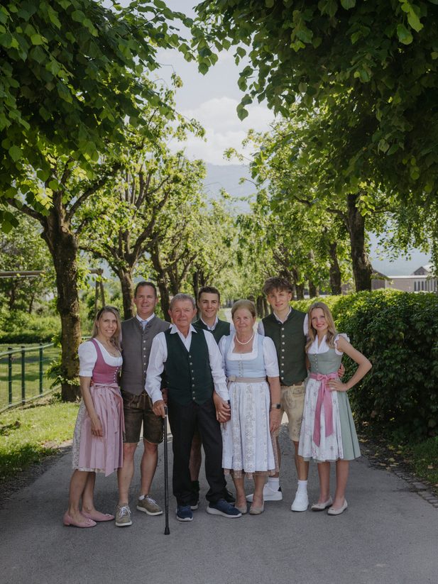 Familie in Tracht auf einem Weg zwischen Bäumen und Hecken im Gartenbereich.
