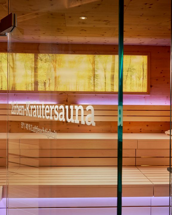 Interior view of a herbal sauna with wooden benches, glass front and indirect LED lighting.