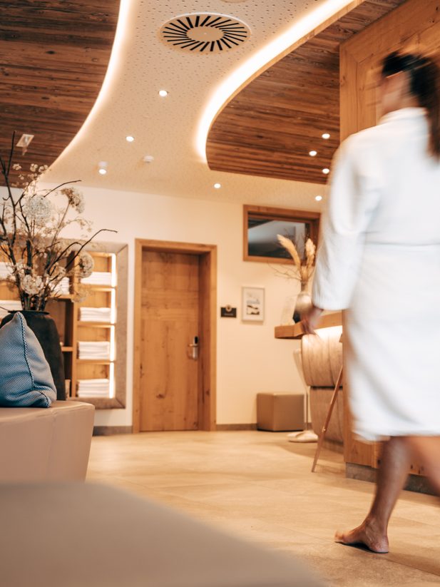 Guest in a bathrobe walking through a wellness area with lounge bench and drink station.