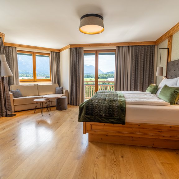 Bright hotel room with double bed, seating area and balcony door with mountain view.