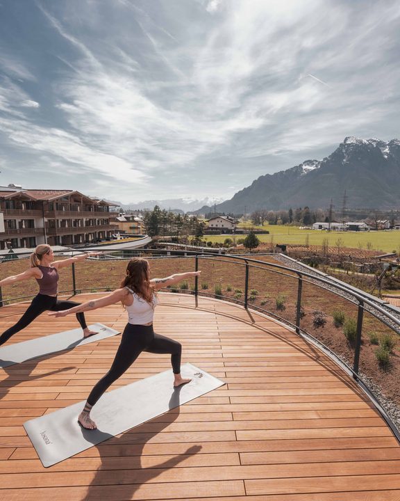 Zwei Gäste machen Yoga auf einer Holzterrasse mit Bergpanorama im Hintergrund.
