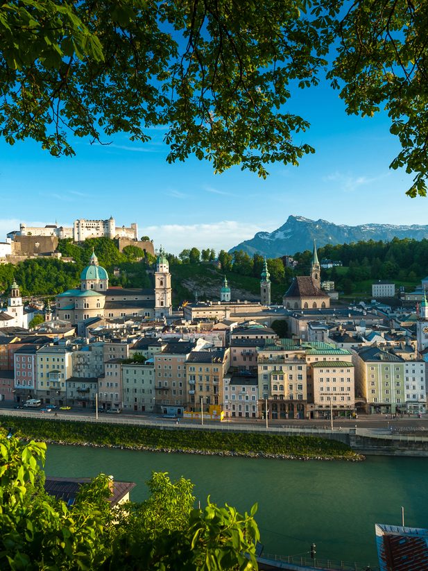 Panoramic view of Salzburg old town with Hohensalzburg Fortress and the Salzach river in the foreground.