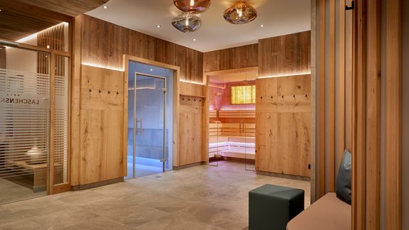 Spa changing area with wood paneling, bench seating, coat hooks, and glass doors to the sauna.