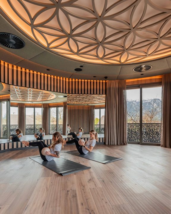 Gäste machen Yogaübungen auf Matten in einem Kursraum mit Panoramafenstern und Bergblick.