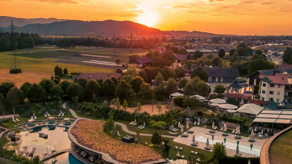 Aerial view of a spa and pool complex at sunset with sun loungers, buildings and surrounding countryside.